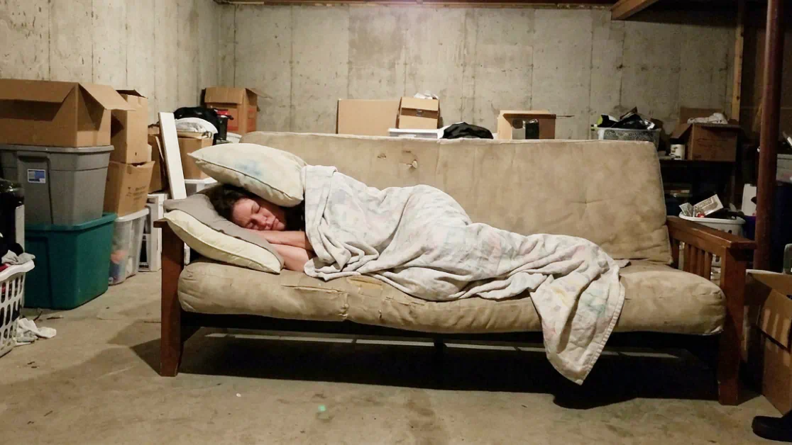 Wife curled up on a basement futon with pillows over her ears